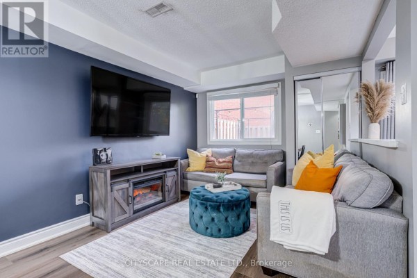 Living room with a grey sofa, teal ottoman, television above an electric fireplace, and a glimpse of mirrored closet doors. - 69 - 45 Wylie Circle, Halton Hills