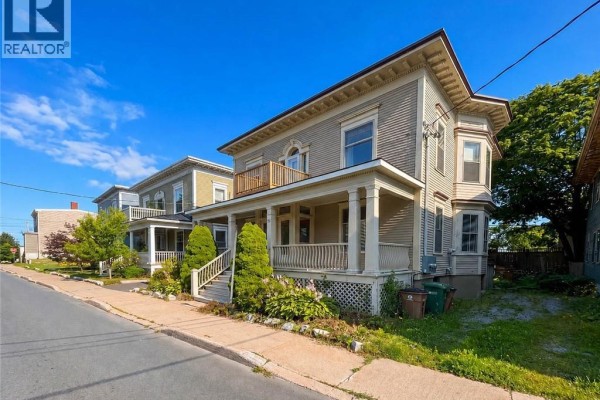 Side view of a two-story beige house with a covered porch and bay window. - 69-71 Clarendon, Saint John