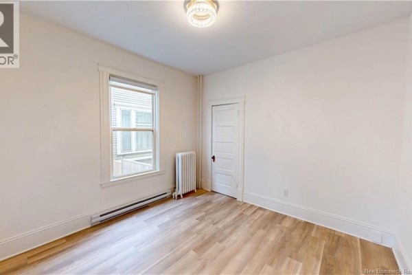 Interior bedroom with light wood laminate flooring, a window, and a radiator. - 69-71 Clarendon, Saint John
