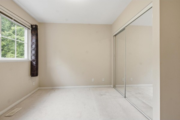 Empty bedroom with a window, beige walls, and a mirrored closet door. - 69 8888 151 Street, Surrey