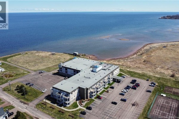 Aerial view of the apartment building from a distance, with waterfront and surrounding landscape. - 69 Cap Bimet Boulevard Unit# 111, Grand Barachois