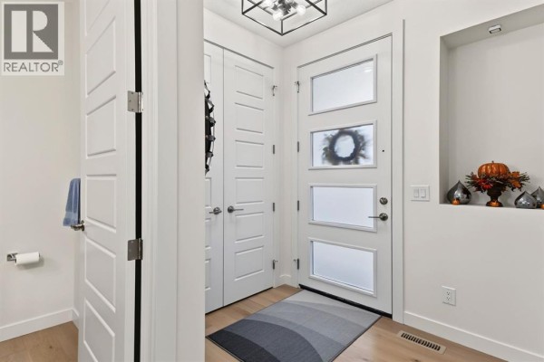 Interior entryway with white doors, light wood floors, and a modern glass front door. - 69 Cobbleridge Place Sw, Airdrie