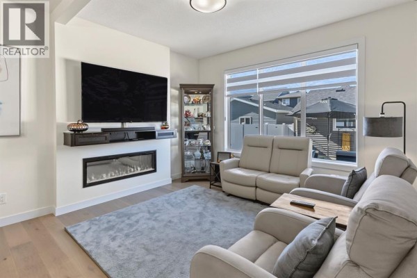 Living room with a fireplace, large television, grey rug, and large window with blinds. - 69 Cobbleridge Place Sw, Airdrie