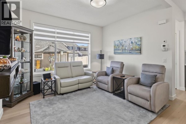 Living room with two recliners, a sofa, grey rug, and large window overlooking the backyard. - 69 Cobbleridge Place Sw, Airdrie