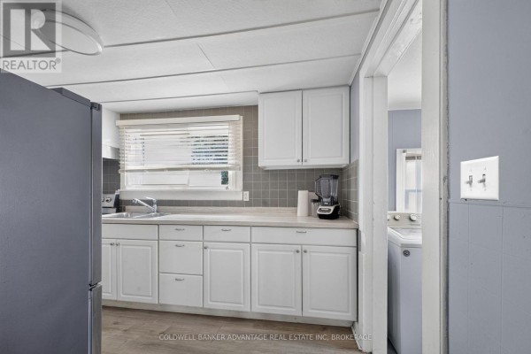 Kitchen area with white cabinets, grey tile backsplash, stainless steel appliances, and a large grey refrigerator. - 69 Dolphin Street, Port Colborne