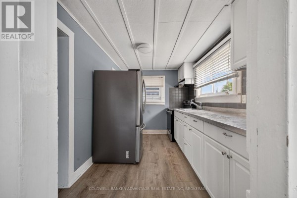 Kitchen with white cabinets, a grey tile backsplash, stainless steel sink, grey refrigerator, and a view of a washer and dryer. - 69 Dolphin Street, Port Colborne