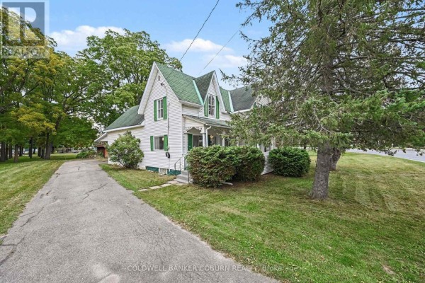 Side view of a white house with green shutters and a green roof, next to a paved driveway. - 69 Main Street, North Dundas