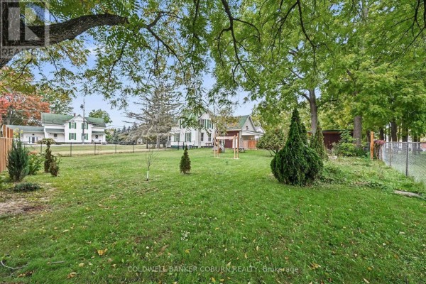Backyard view of a white house with green shutters, a play structure, and mature trees. - 69 Main Street, North Dundas