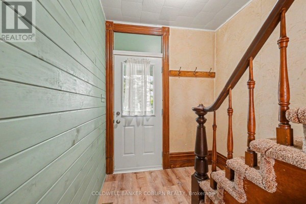Interior view of a home entrance, showing a white door, wood trim, and a carpeted staircase. - 69 Main Street, North Dundas