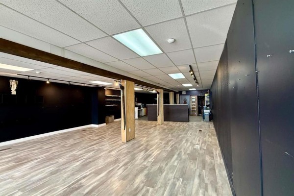 Empty commercial interior with light wood laminate flooring, dark walls, and exposed wooden beams. - 69 Main Street S, Minnedosa
