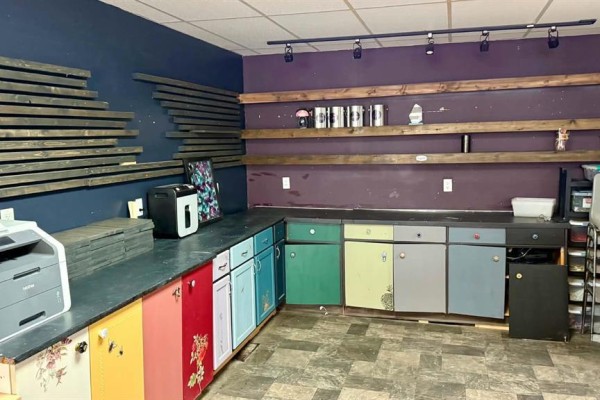 Work area with colorful cabinets, dark countertops, shelving, and a printer on the left. - 69 Main Street S, Minnedosa