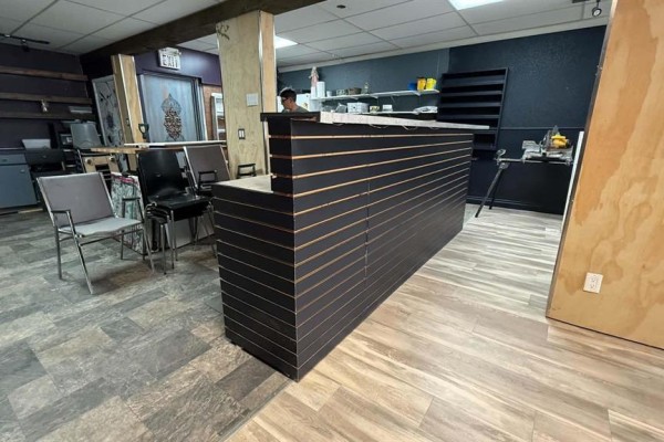 Dark slatted reception desk in an empty commercial space with chairs and shelving in the background. - 69 Main Street S, Minnedosa
