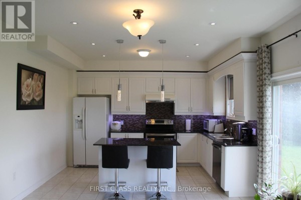 White kitchen with granite countertops, island with seating, and stainless steel appliances. - 69 Promenade Drive, Whitby