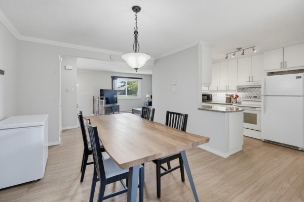 Open concept dining area with a light wood table and chairs, adjacent to a light grey living room and white kitchen. - 69 Rue De Piedmont, Gatineau
