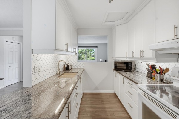 L-shaped kitchen with white cabinets, granite countertops, stainless steel sink, and white appliances, overlooking a living area. - 69 Rue De Piedmont, Gatineau