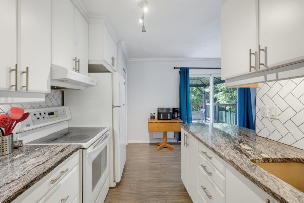 Kitchen with white cabinets, granite countertops, stainless steel appliances, and a pass-through window to a dining area. - 69 Rue De Piedmont, Gatineau