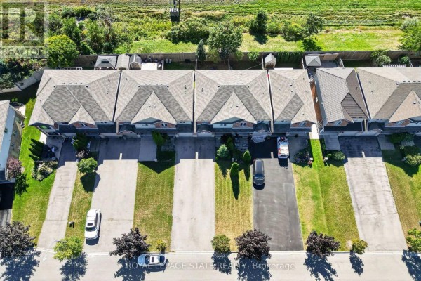 Aerial view of a residential neighborhood with townhouses, pools, green spaces, and a distant lake. - 69 Sumner Crescent, Grimsby