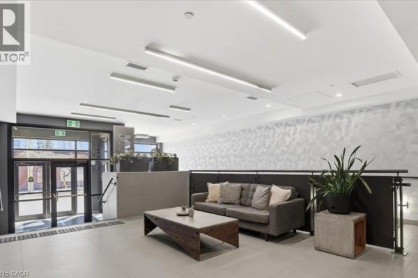 Apartment building lobby with a gray sofa, coffee table, plants, and minimalist lighting. - 690 King Street W Unit# 214, Kitchener