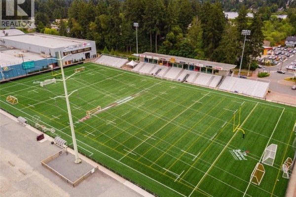 Drone view of a large artificial turf sports field with goalposts and stadium seating. - 690 Madrona Ridge, Langford