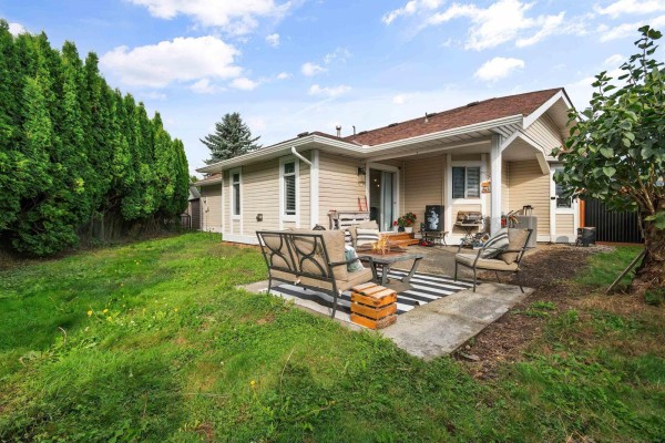 Backyard patio with seating, a fire pit, and surrounded by a lawn and mature trees. - 6900 Oakwood Drive, Agassiz, Agassiz