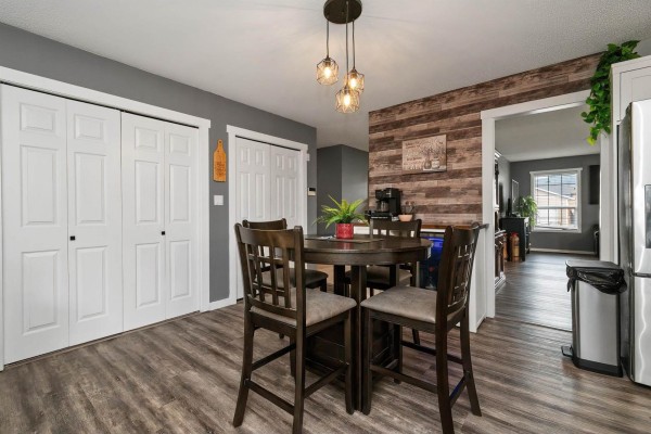Dining area with a round table, view into hallway, and wood-plank accent wall next to white double doors. - 6900 Oakwood Drive, Agassiz, Agassiz
