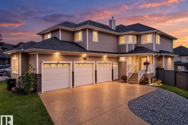 Front exterior of the house at dusk, illuminated by interior and exterior lights. - 6904 18 Av Sw, Edmonton