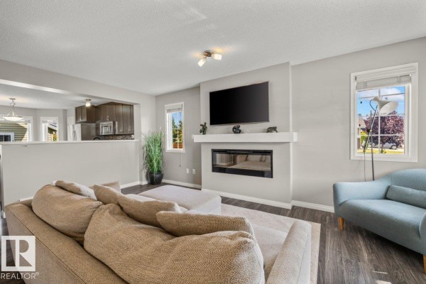 Living room with a beige sectional sofa, ottoman, electric fireplace, and television mounted above the mantel. - 6906 23 Av Sw, Edmonton