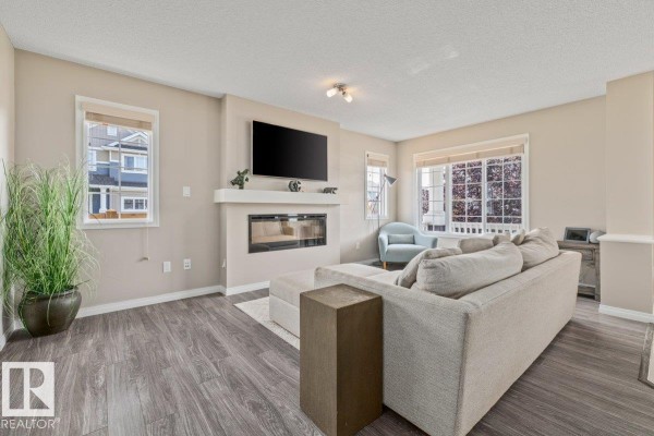 Living room with a sectional sofa, blue armchair, electric fireplace, and television mounted on the wall. - 6906 23 Av Sw, Edmonton