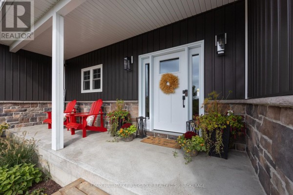 Covered front porch with two red adirondack chairs, planters, and a white front door with a wreath. - 6909 Battersea Road, Frontenac