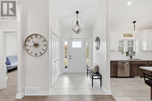 Bright entryway with tile flooring, a large wall clock, white doors, a bench, and view into the kitchen. - 6909 Battersea Road, Frontenac