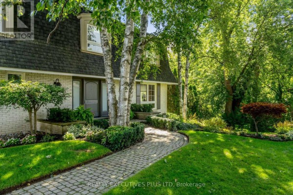 Stone pathway curves through a green lawn towards the entrance of a house with birch trees. - 691 Nautalex Court, Mississauga