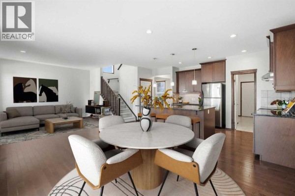 Open concept living and dining area with a fireplace, view of the kitchen and staircase. - 691 Panamount Boulevard Nw, Calgary