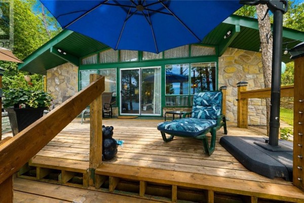 Deck with patio furniture and a stone-clad building with large windows and sliding doors. - 692 Old Village Rd., Birch Island