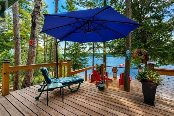 Outdoor seating area on a wooden deck with water and tree views. - 692 Old Village Rd., Birch Island
