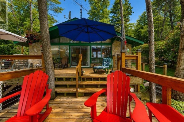 Deck with red Adirondack chairs and a view of a cottage and lake. - 692 Old Village Rd., Birch Island