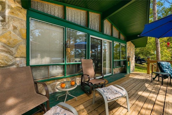 Close-up of a deck with patio chairs and a stone building with green trim. - 692 Old Village Rd., Birch Island