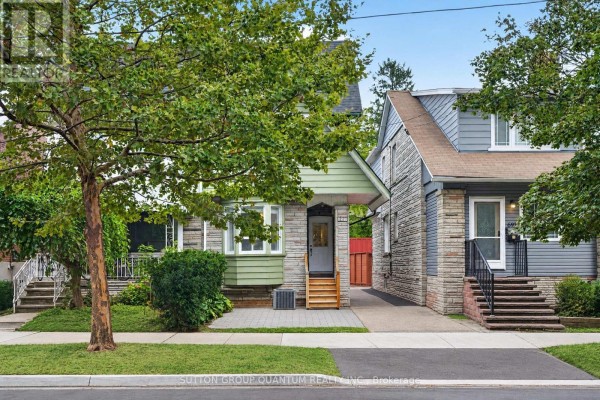 Exterior view of a narrow house with green siding, stone accents, and a covered front entrance. - 693 Greenwood Avenue, Toronto