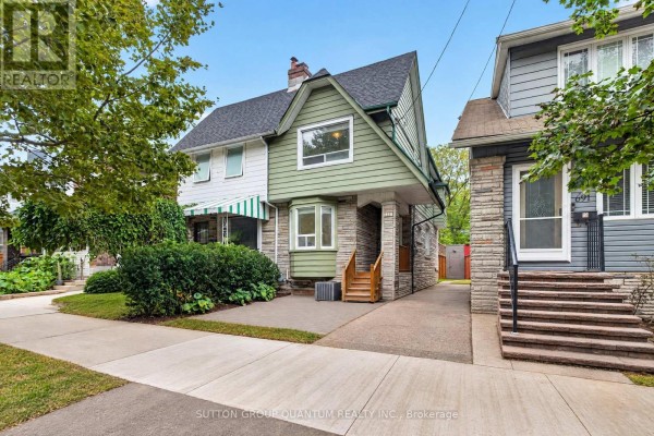 Side view of a green and stone house with large trees and a driveway. - 693 Greenwood Avenue, Toronto