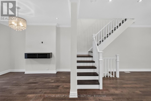 Interior view of a living room with dark wood floors, a white staircase, and neutral walls. - 693 Greenwood Avenue, Toronto