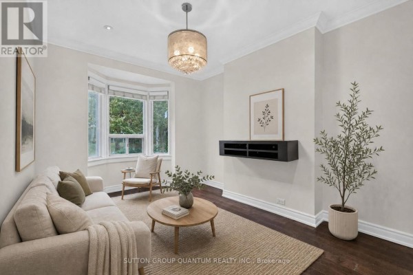 Living room with a bay window, light-colored sofa, round coffee table, and wall-mounted media console. - 693 Greenwood Avenue, Toronto