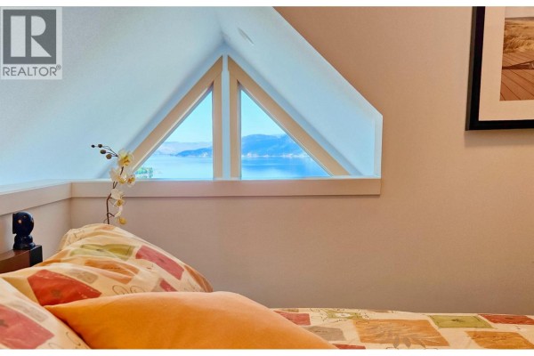 Bedroom with a queen-size bed, bedside table, lamp, sloped ceiling, and framed artwork. - 6931 Barcelona Drive Unit# 62, Kelowna
