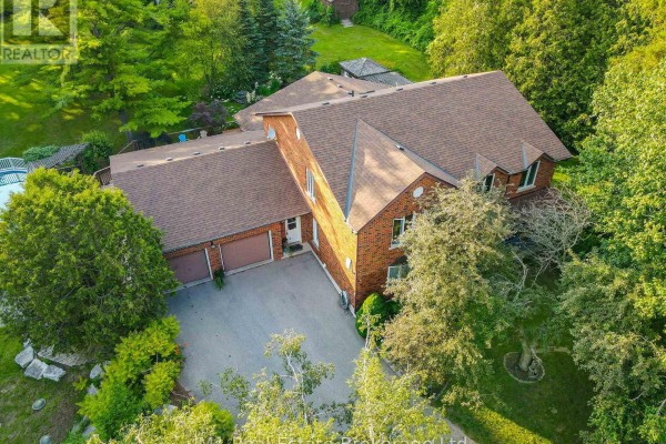Front view of a brick house with a connected three-car garage and lush landscaping. - 6946 Fife Road, Guelph/eramosa
