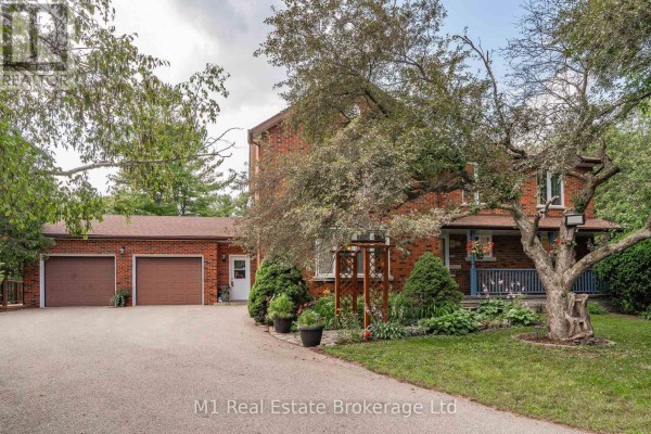 Curving driveway leading to a brick house with a three-car garage and front porch. - 6946 Fife Road, Guelph/eramosa