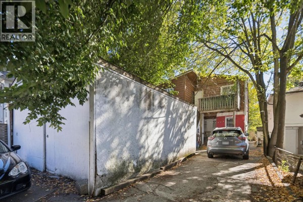 Rear alleyway with a white stucco wall, a parked car, and the back of a house. - 695 E 12th Avenue, Vancouver