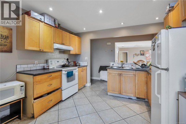 Kitchen with light wood cabinets, white appliances, tiled floor, and dark laminate countertops. - 695 Franklyn St, Nanaimo