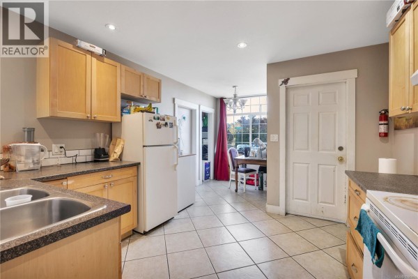 Kitchen view showing double sink, white refrigerator, and doorway to dining area with red curtains. - 695 Franklyn St, Nanaimo