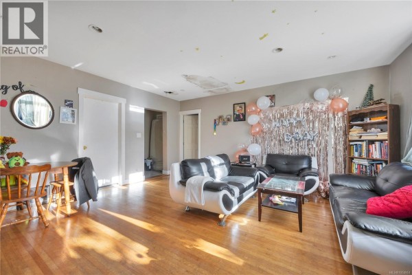 Living room with hardwood floors, black and white sofas, a small dining set, and built-in shelving. - 695 Franklyn St, Nanaimo