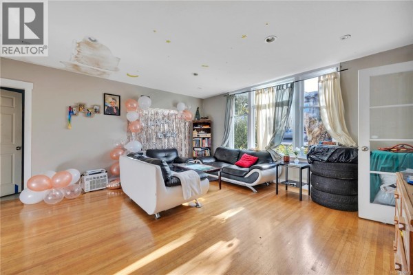 Spacious living room with hardwood floors, large windows, leather sofas, and party decorations on walls. - 695 Franklyn St, Nanaimo