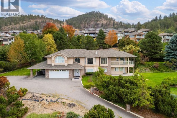 Front view of a beige house with a long driveway, attached garage, and covered carport. - 695 Valley Road, Kelowna