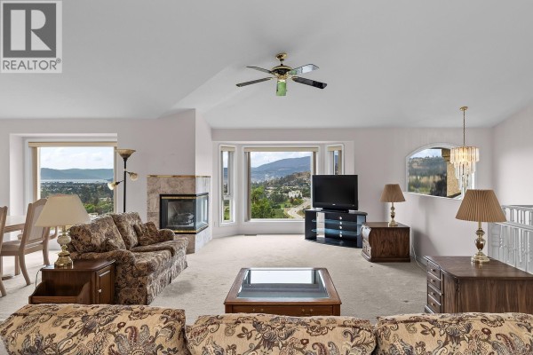 Living room with floral sofas, fireplace, large windows with a valley view, and a television. - 695 Valley Road, Kelowna